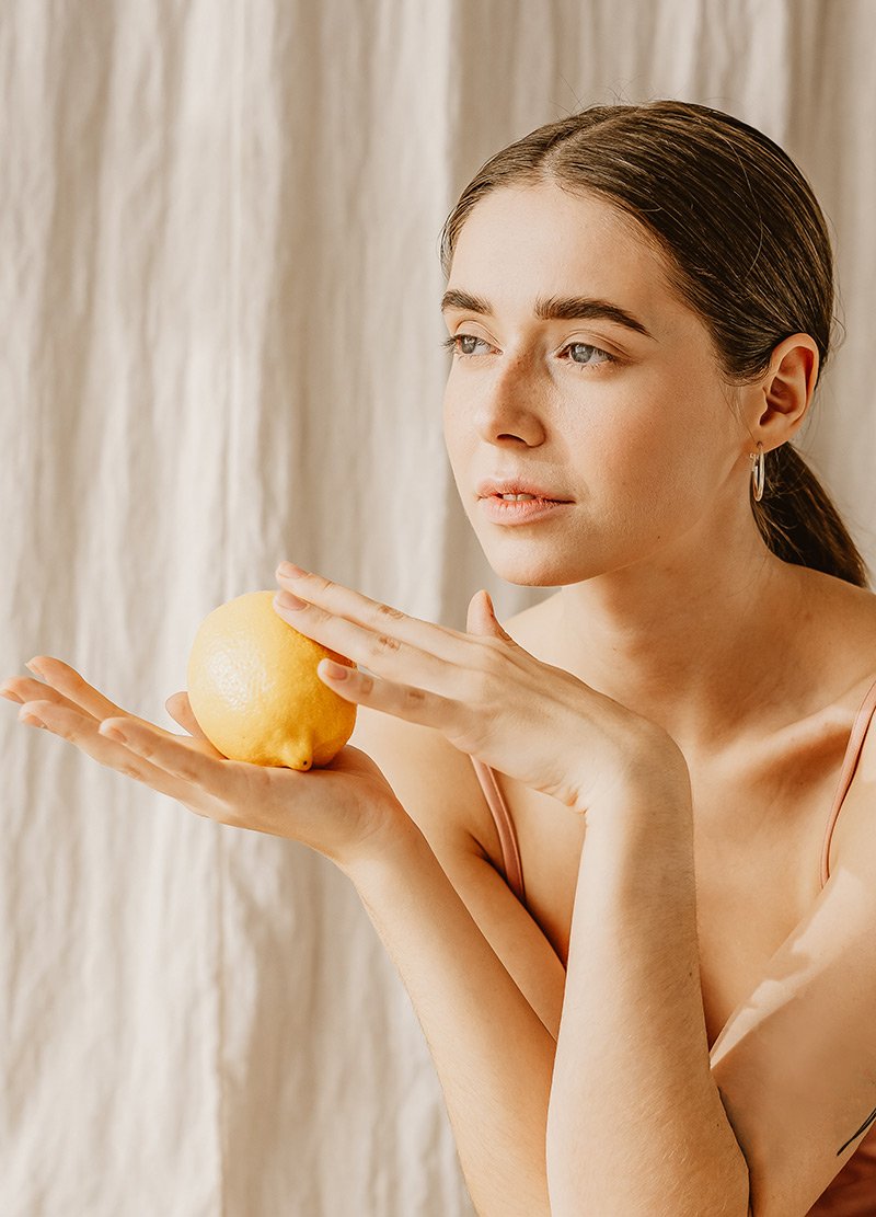 Frau mit frischer Zitrone in der Hand, symbolisiert die Anwendung von Fruchtsäurepeelings für die Gesichtspflege bei RAU Cosmetics.