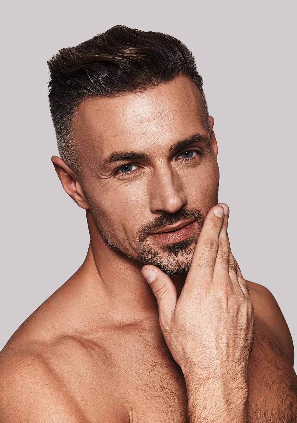 Ein nachdenklicher Mann ohne Hemd, der glatte Haut und gepflegte Gesichtsbehaarung zur Schau stellt und für RAU Cosmetics für Herrenpflege wirbt.