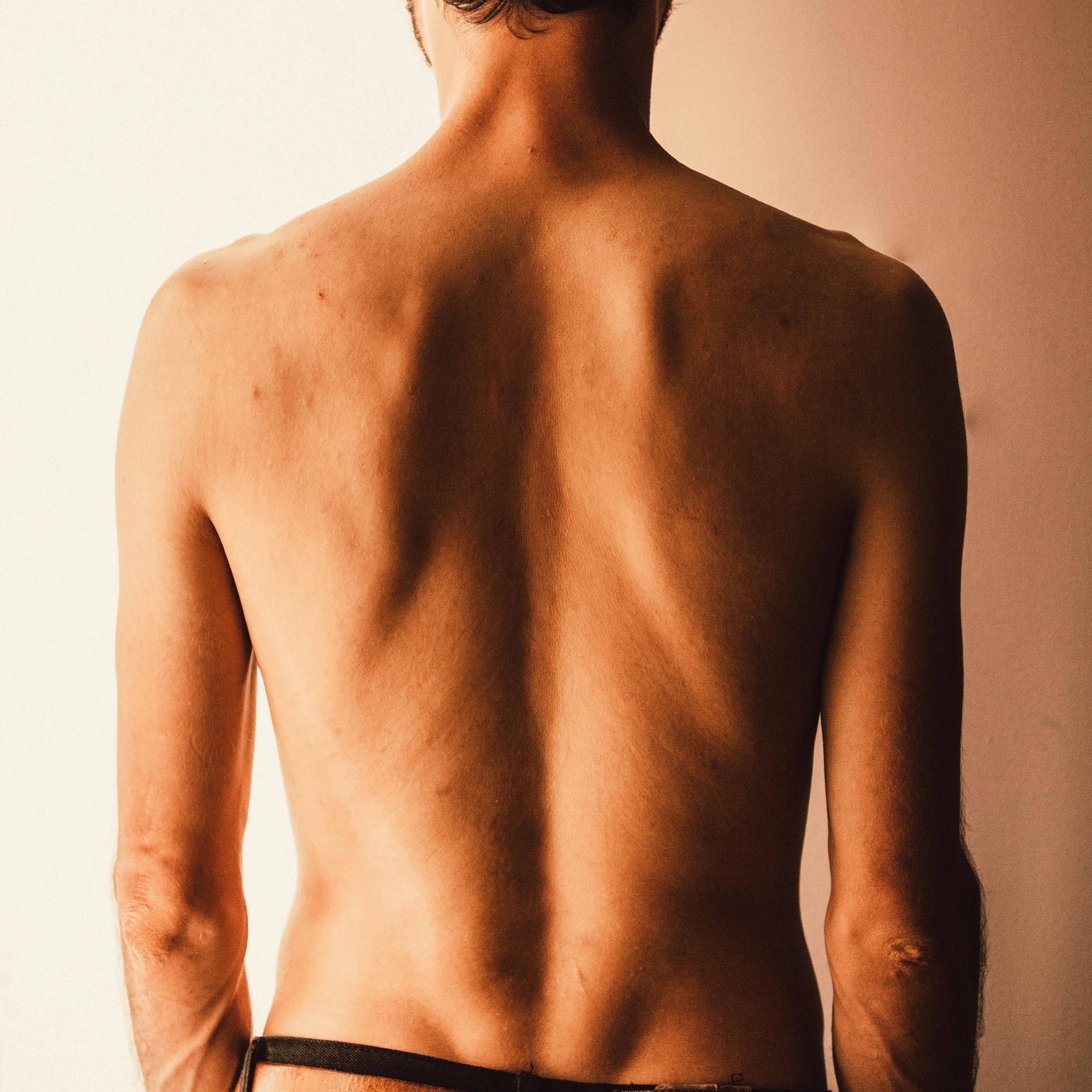 Frau mit Rückenansicht, die sich mit beiden Händen über die Schultern streckt, während sie in einem weißen Badetuch vor einem Spiegel steht.