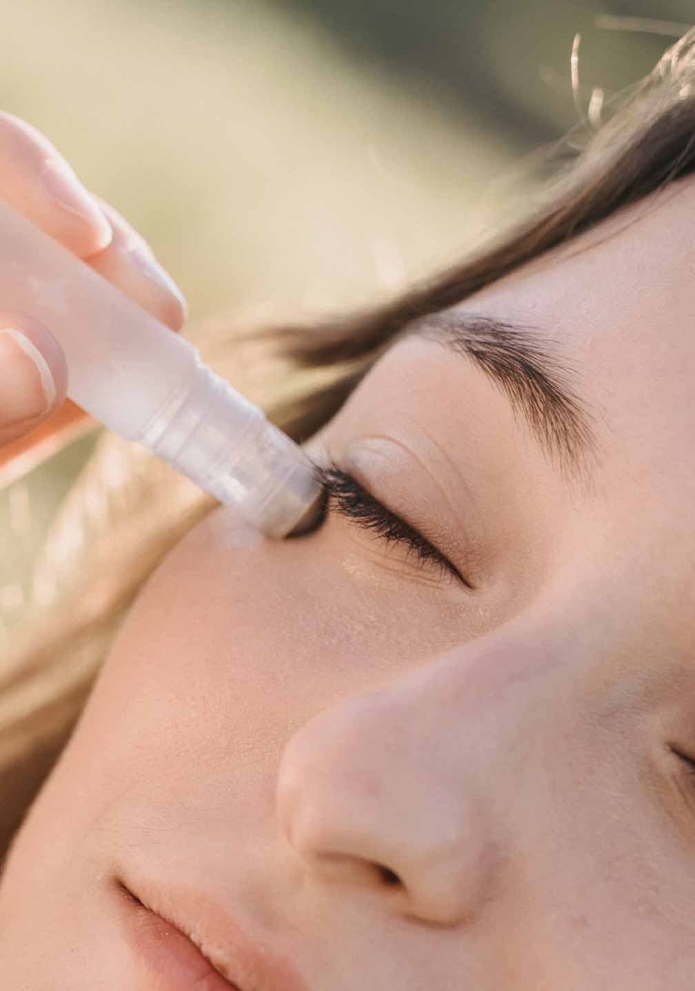 Frau, die RAU Cosmetics Eye Lifting Roll-On aufträgt, mit entspannter Miene. Nahe Ansicht, natürliche Beleuchtung.